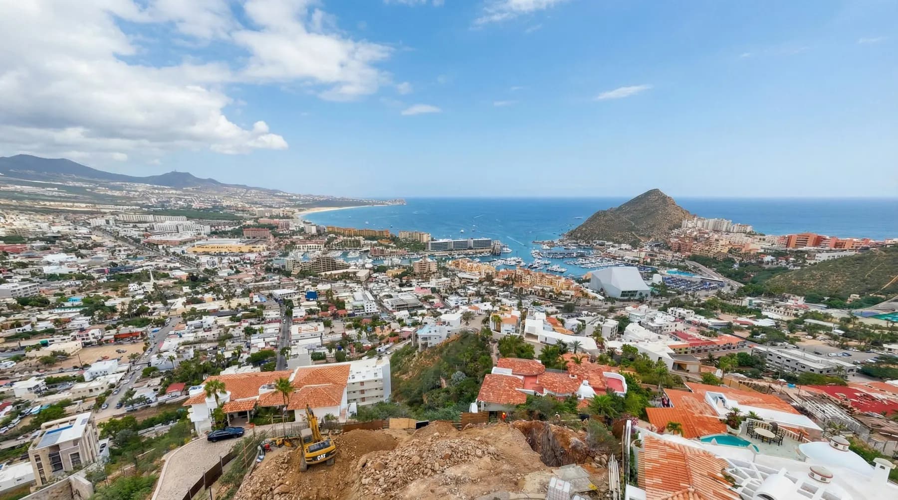 Villa del León under construction in Pedregal — yellow CAT on the hillside, Cabo marina and Land’s End beyond